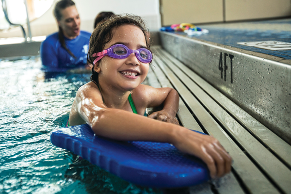 Young girl smiling with goggles on learning how to swim.
