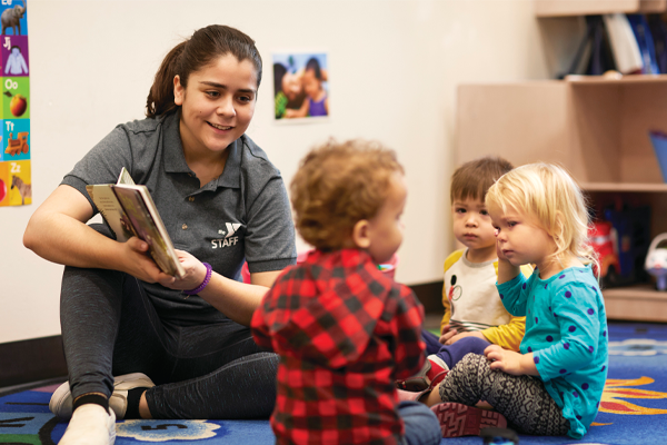 YMCA staff member reading to young toddlers.