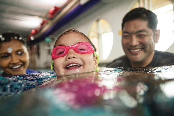 Young girl swimming with her parents.