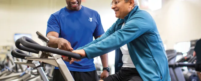 Ymca Staff Member Helping Out A Man On A Fitness Machine.