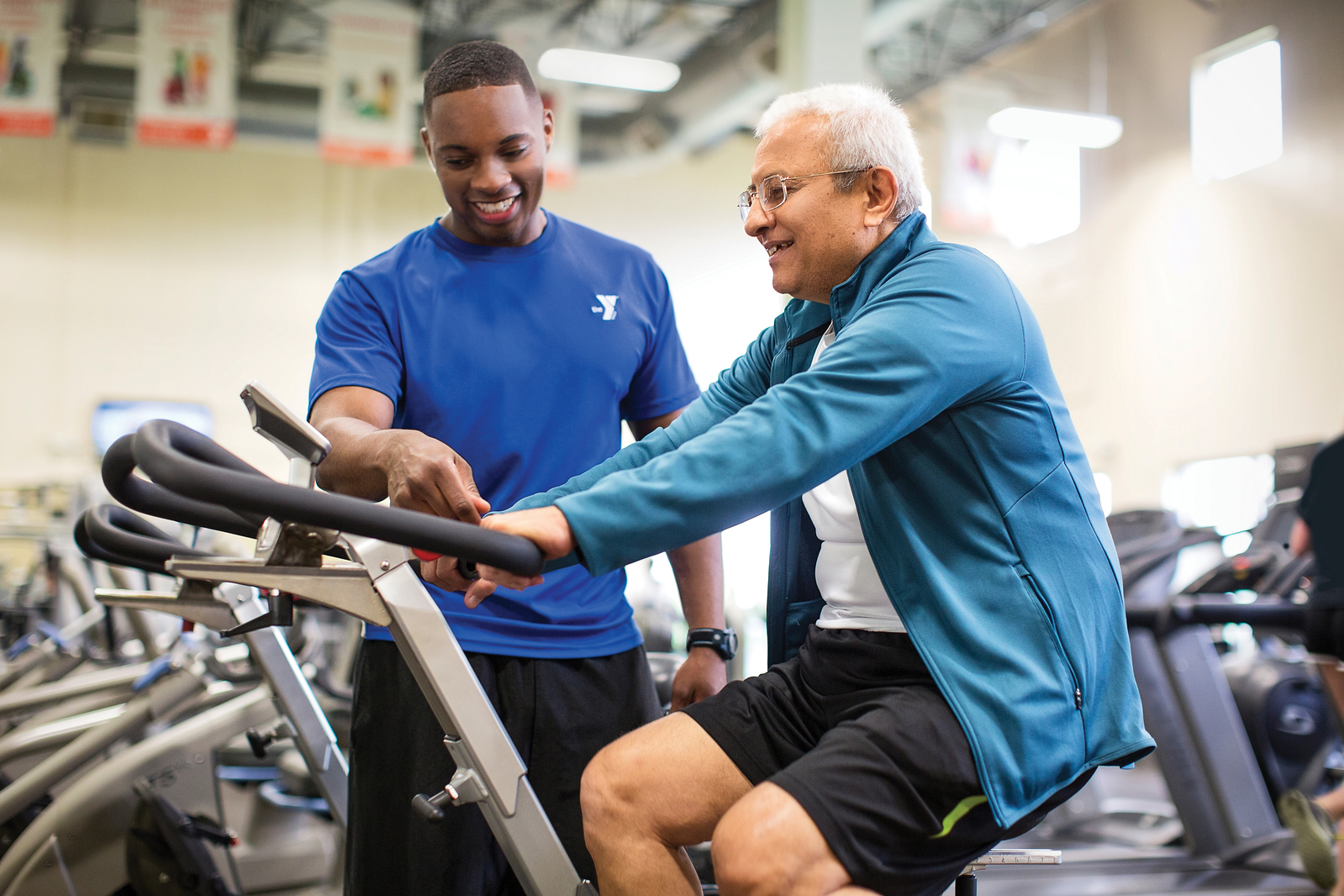 YMCA staff member helping out a man on a fitness machine.