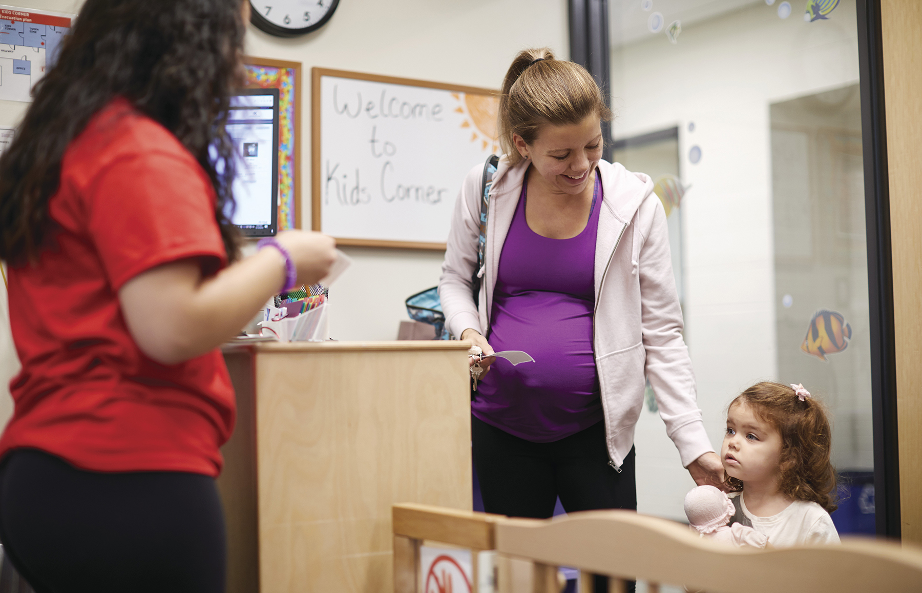 Pregnant mom checking her young toddler into childcare.