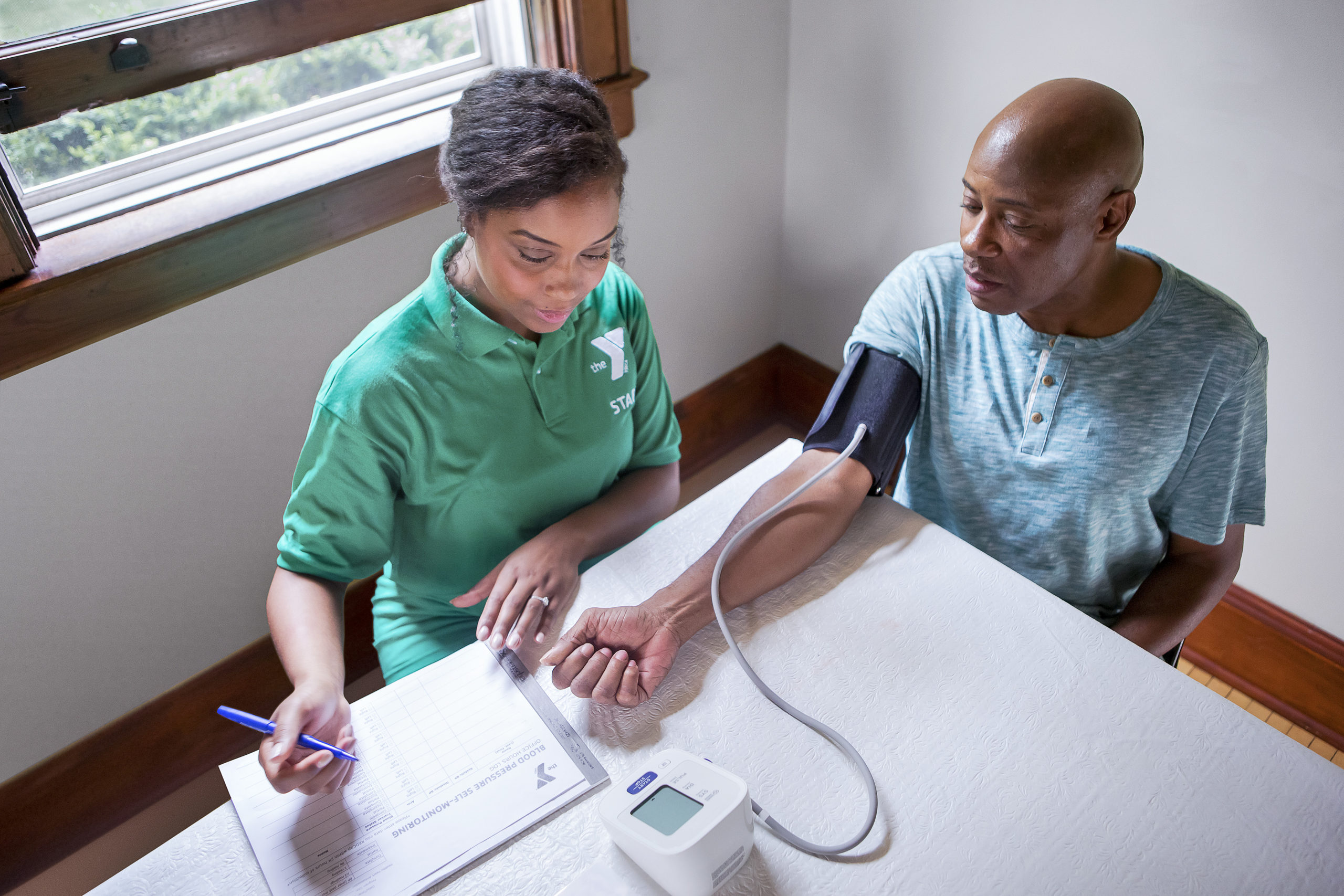 YMCA staff member measuring blood pressure of man.