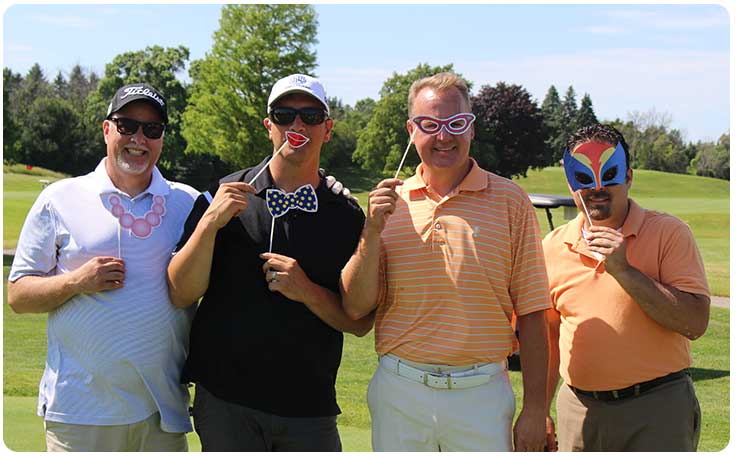 Four men on a golf course smiling and posing with funny accessories.