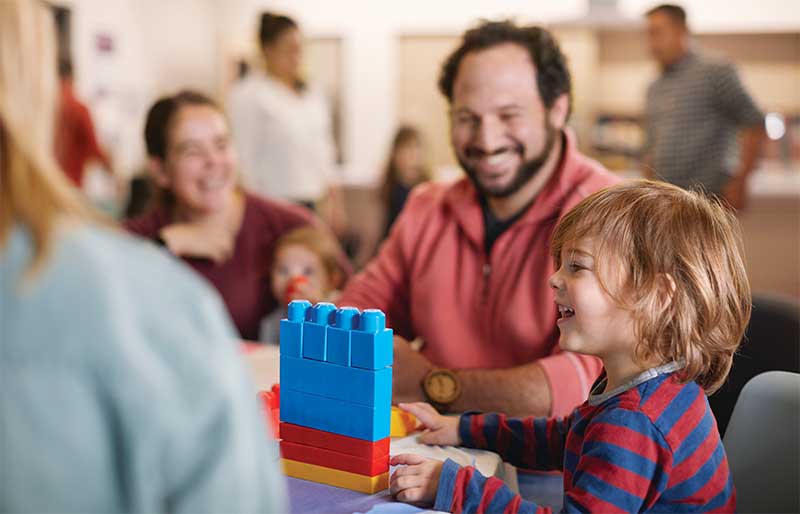 Young boy building legos while parents smile and watch.