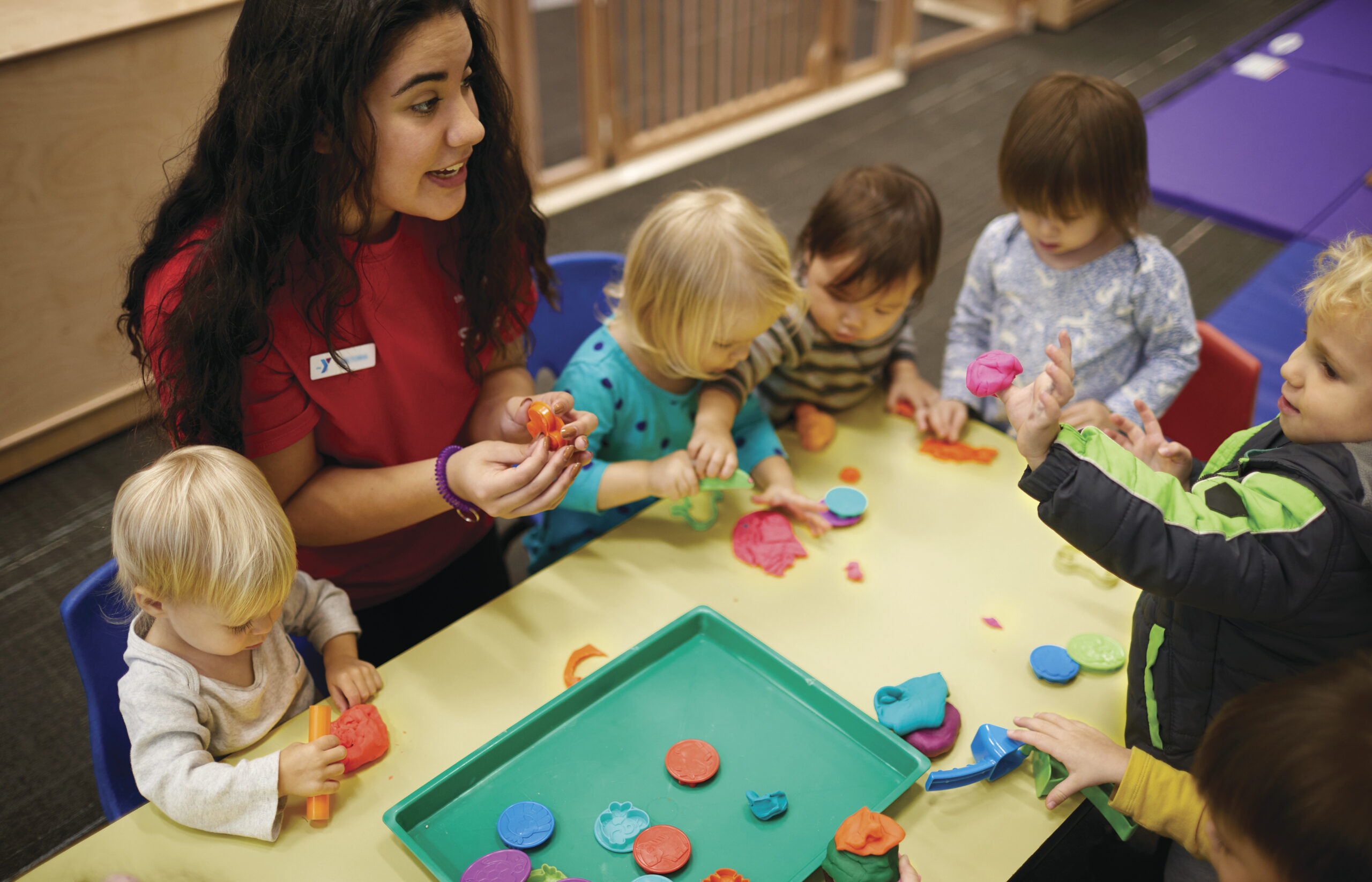 YMCA staff member help little children play with play dough.