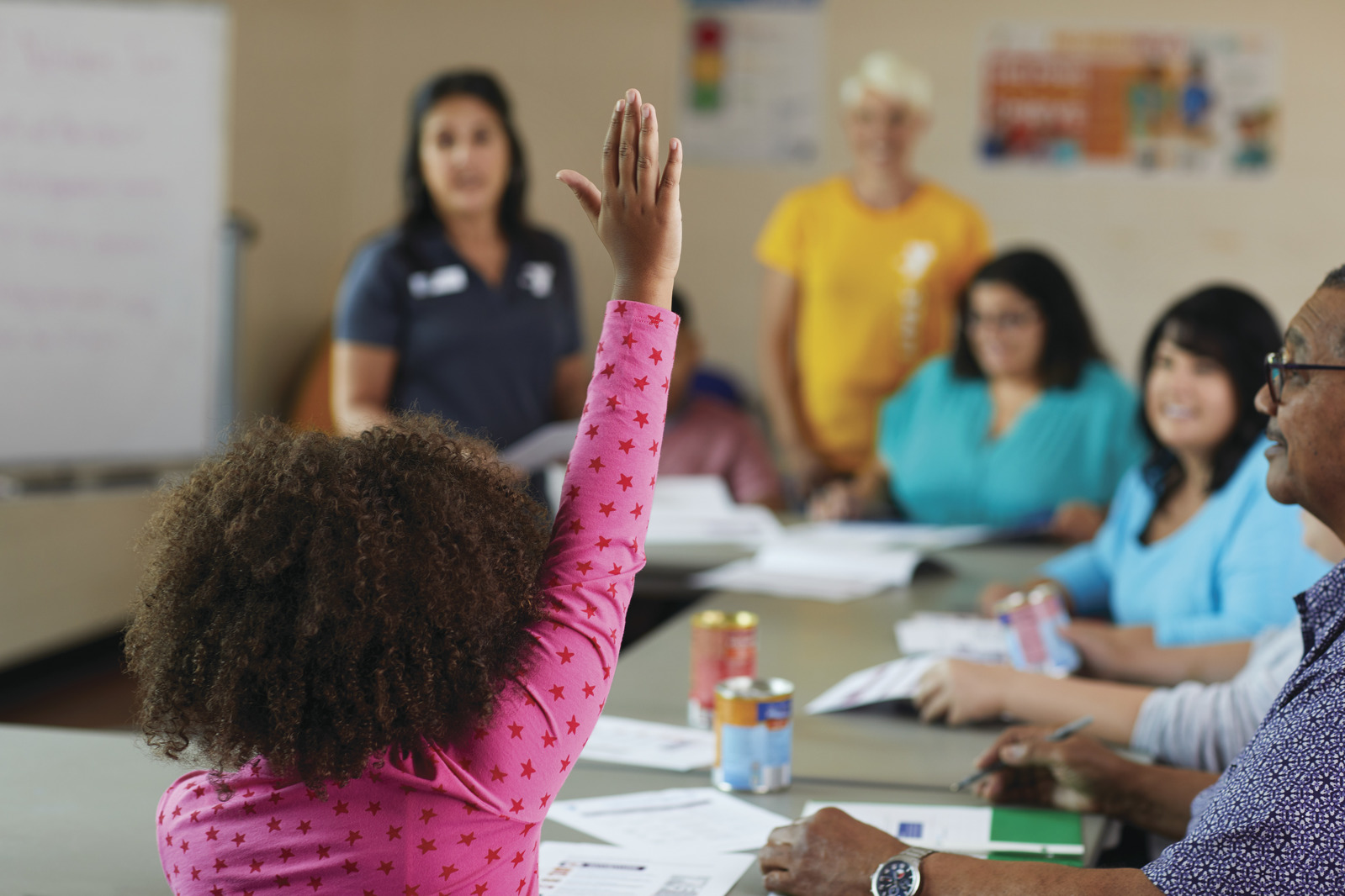 Young girl raising her hands in a room of adults.