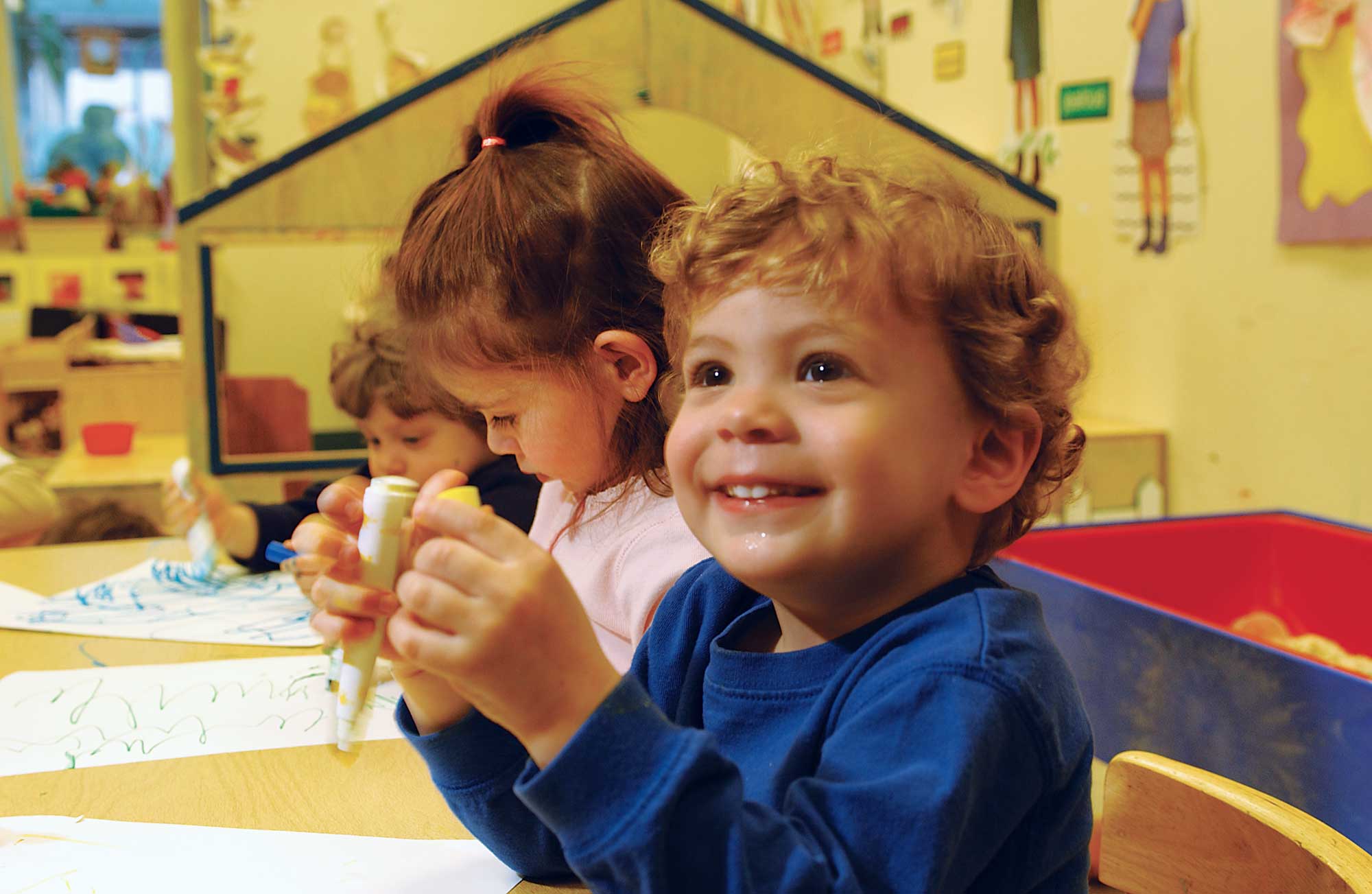 Young preschoolers smiling while coloring with markers.