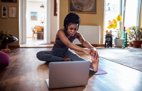 Young women stretching her leg out following along to a YMCA virtual workout in her living room.