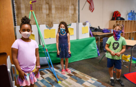 Three children with masks in a fun class room at the YMCA.