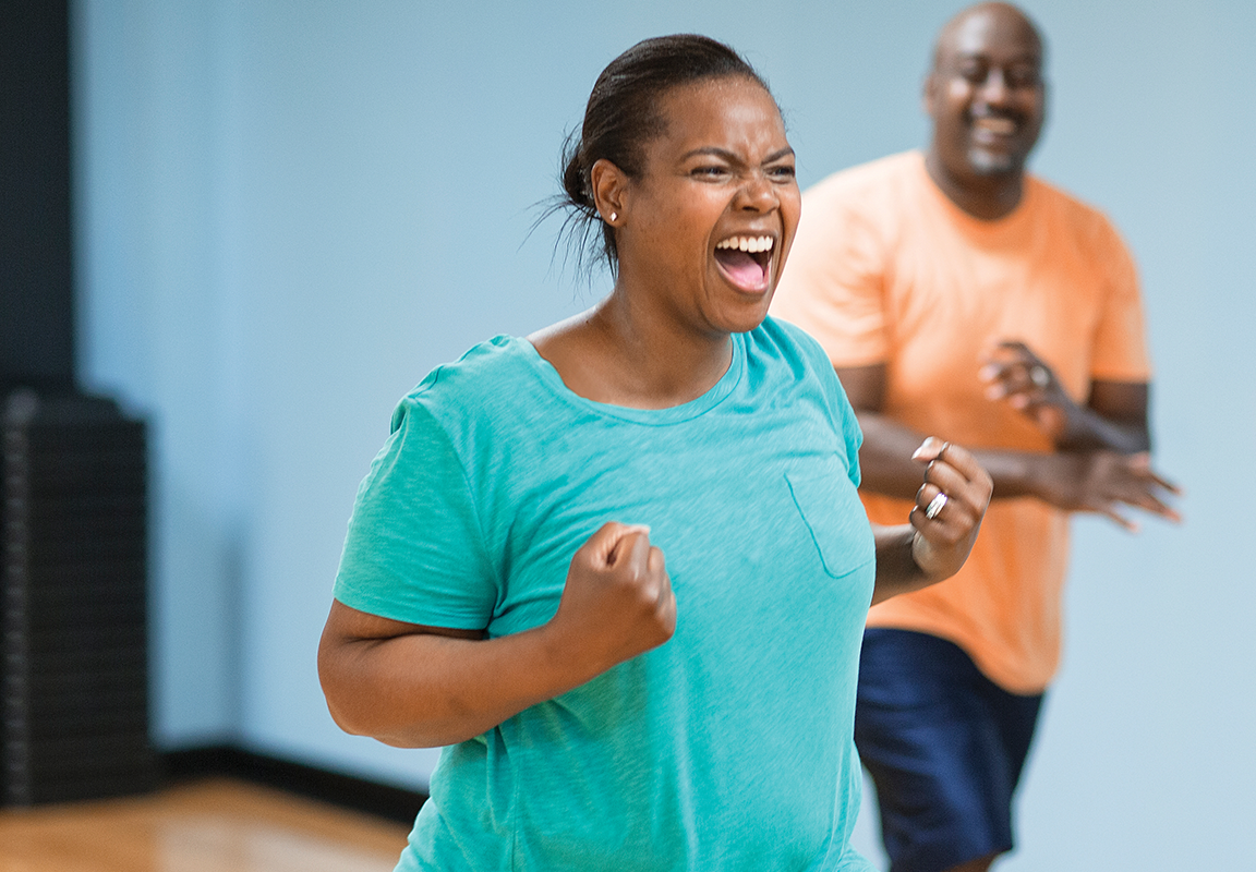Woman having fun while at a fitness class while man is in the back smiling.