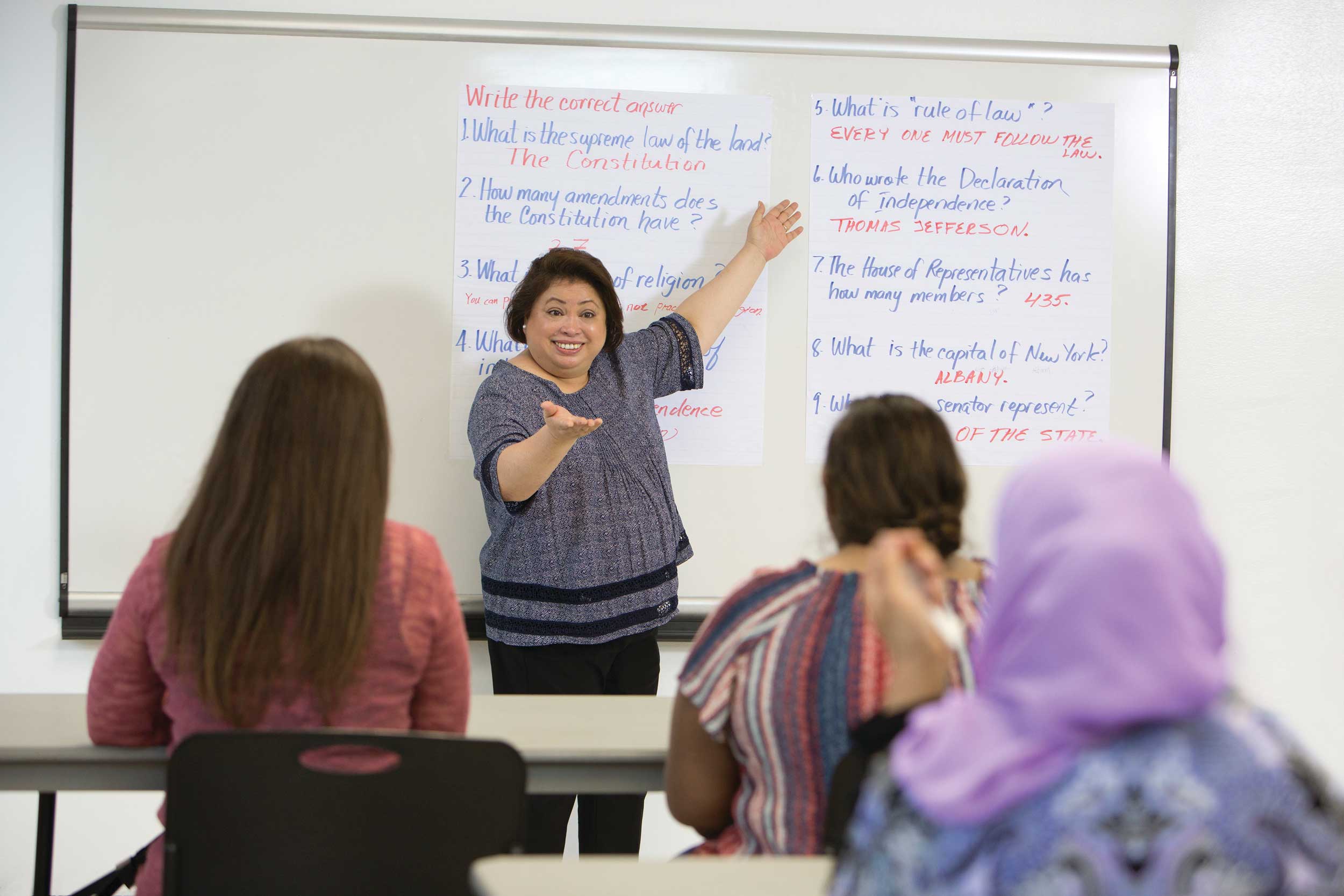 Woman pointing to a whiteboard in front of a classroom