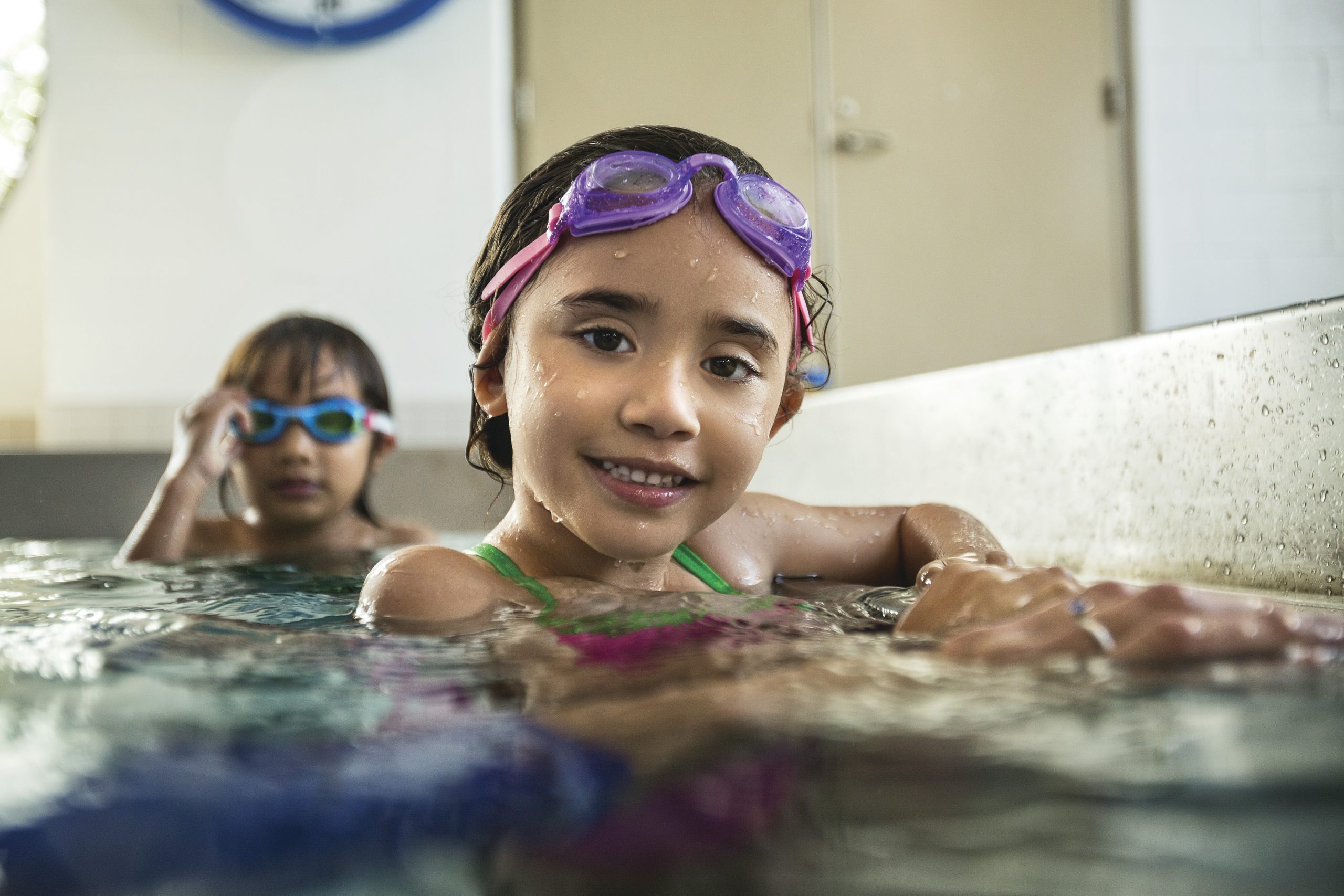 Girls holding on to the side of pool smiling.