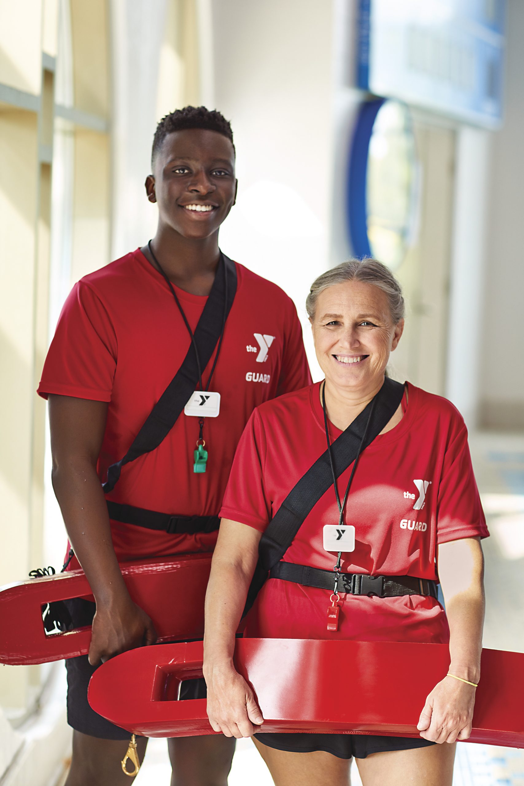 Male and female smiling lifeguards standing next to the YMCA pool with their rescue tubes.