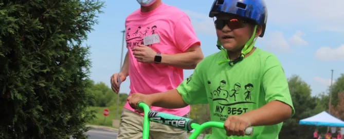 Volunteer Running Next To A Young Boy On Bike For The Tri My Best Triathlon.