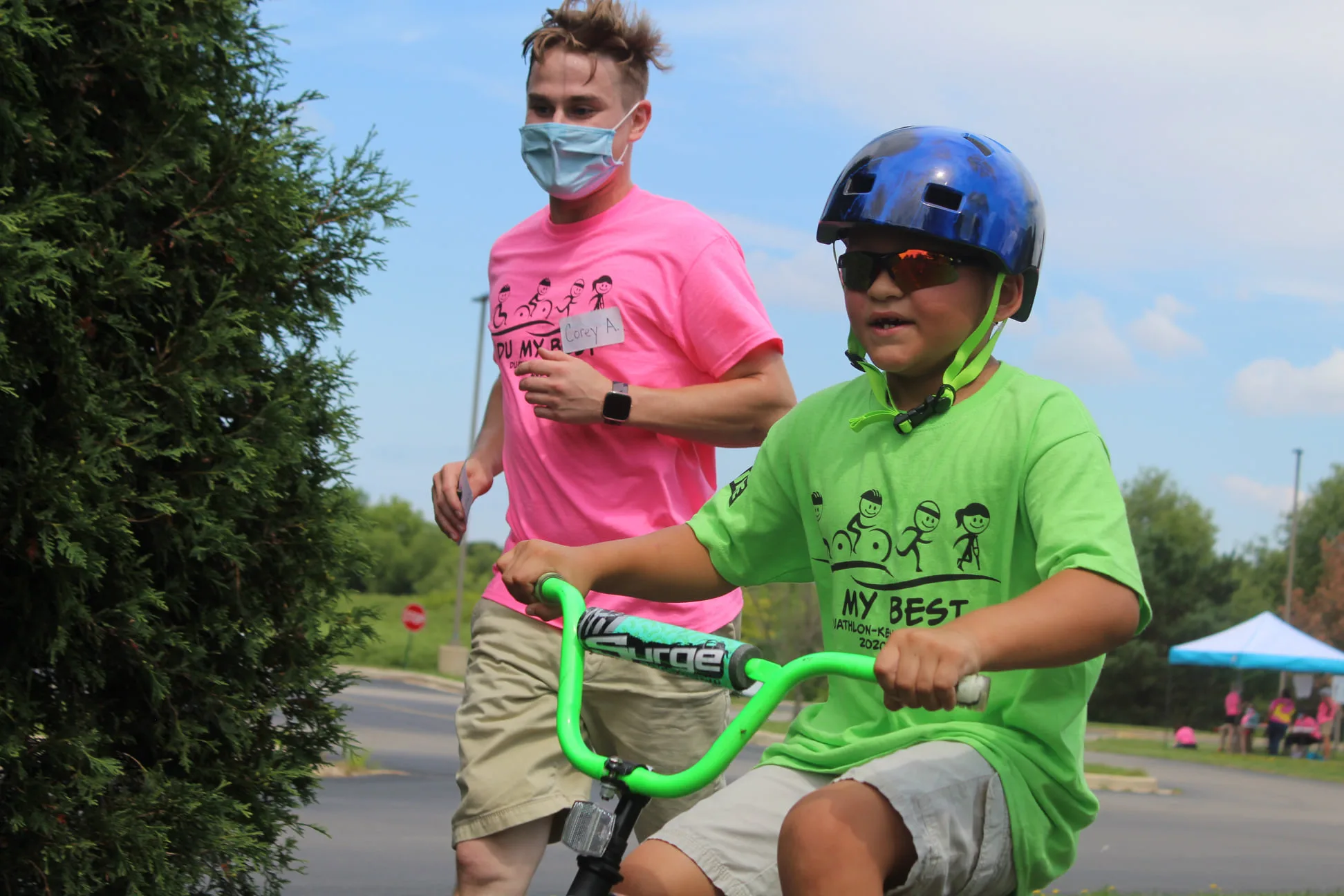 Volunteer Running Next To A Young Boy On Bike For The Tri My Best Triathlon.