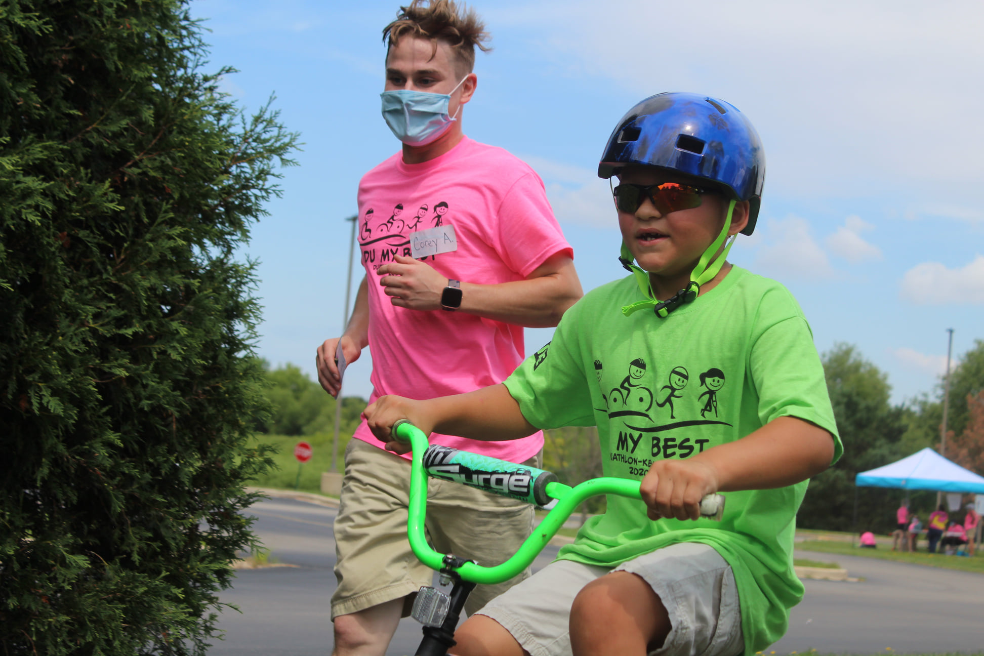 Volunteer running next to a young boy on bike for the Tri My Best Triathlon.