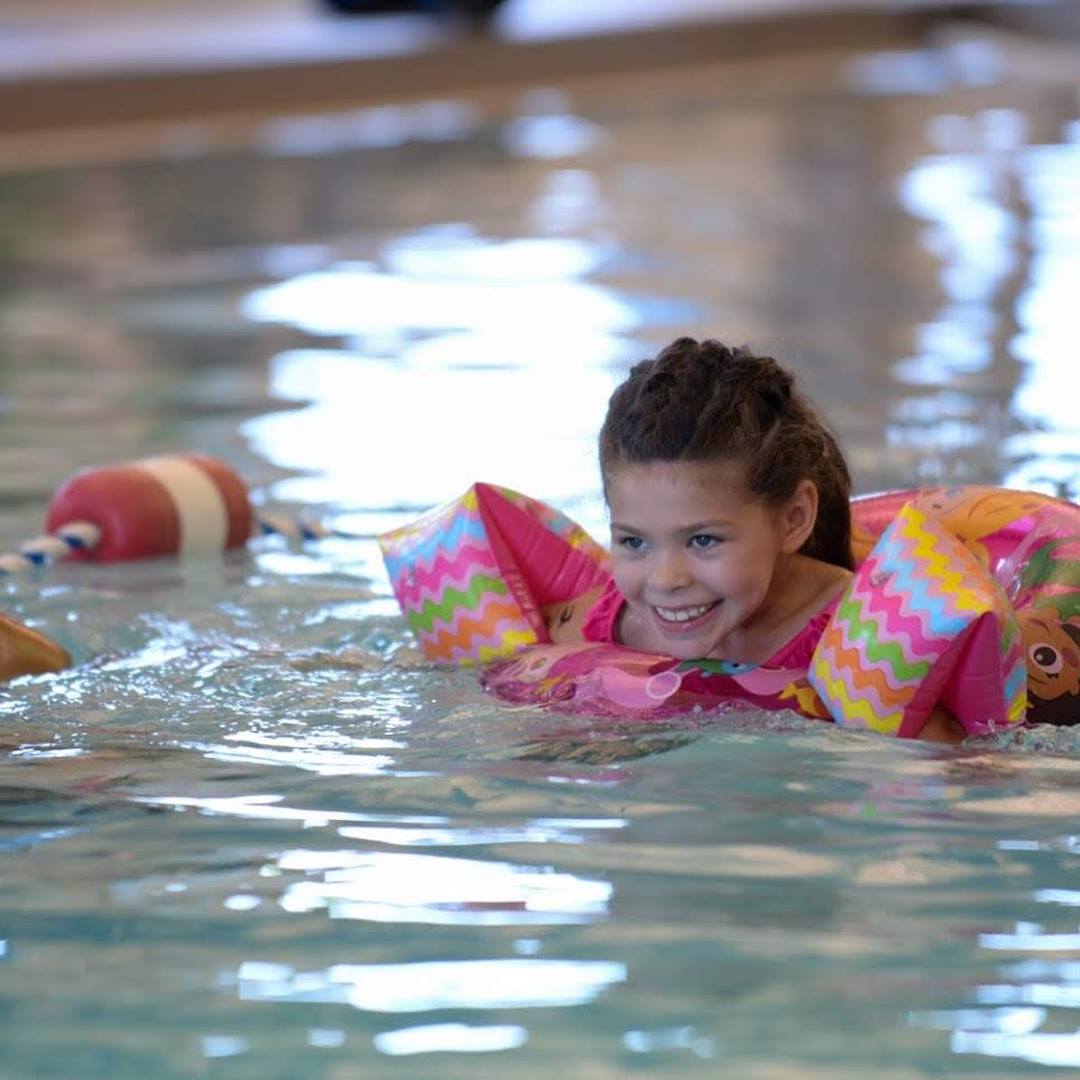 Smiling girl swimming in the YMCA with floaties on.