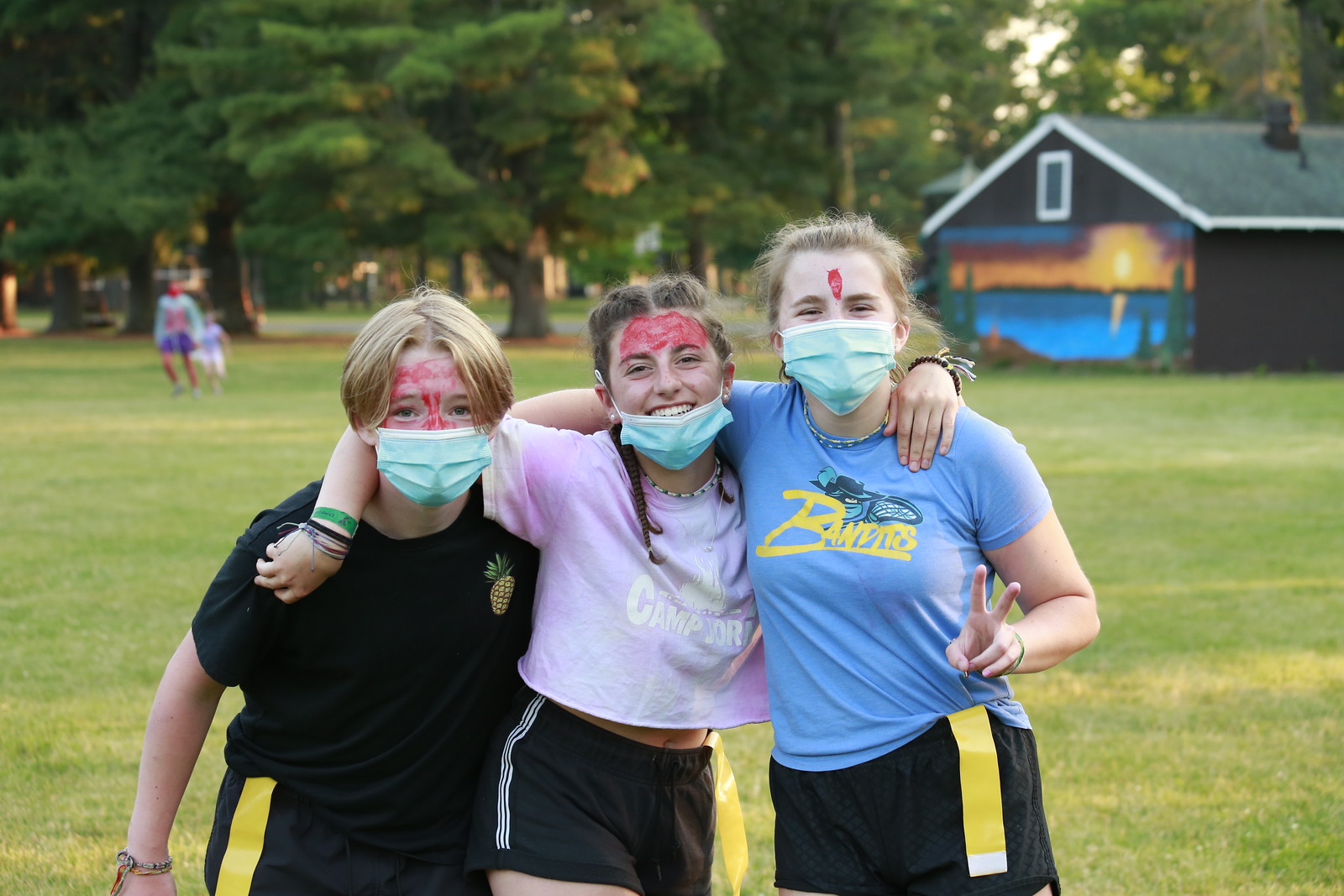 Two girls and a boy smiling and hugging each other with red face paint on at YMCA Camp Jorn.