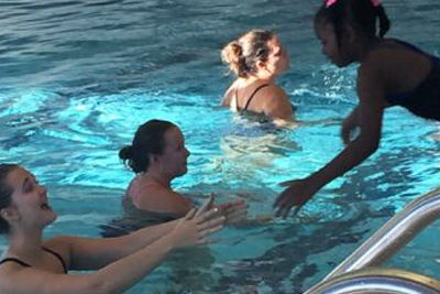 Young girl jumping into a women's arm in the YMCA pool.