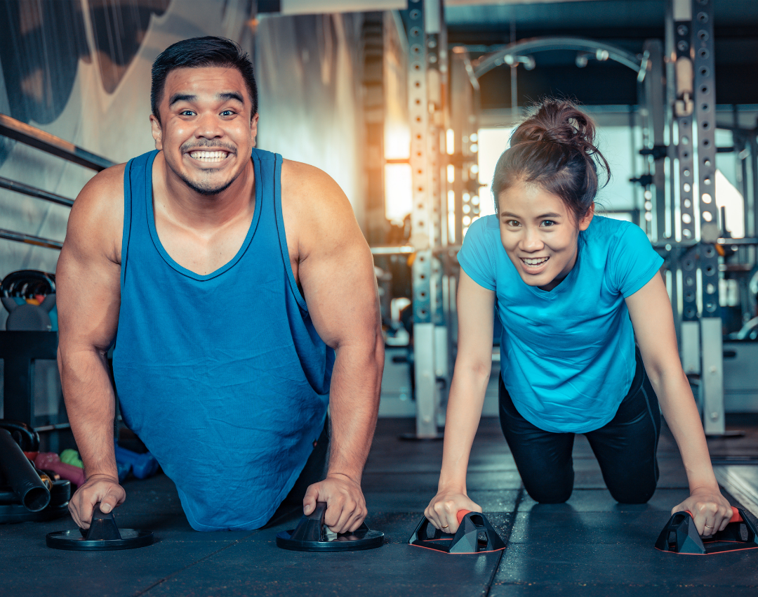 Father and daughter smiling doing push ups together at the YMCA fitness center.