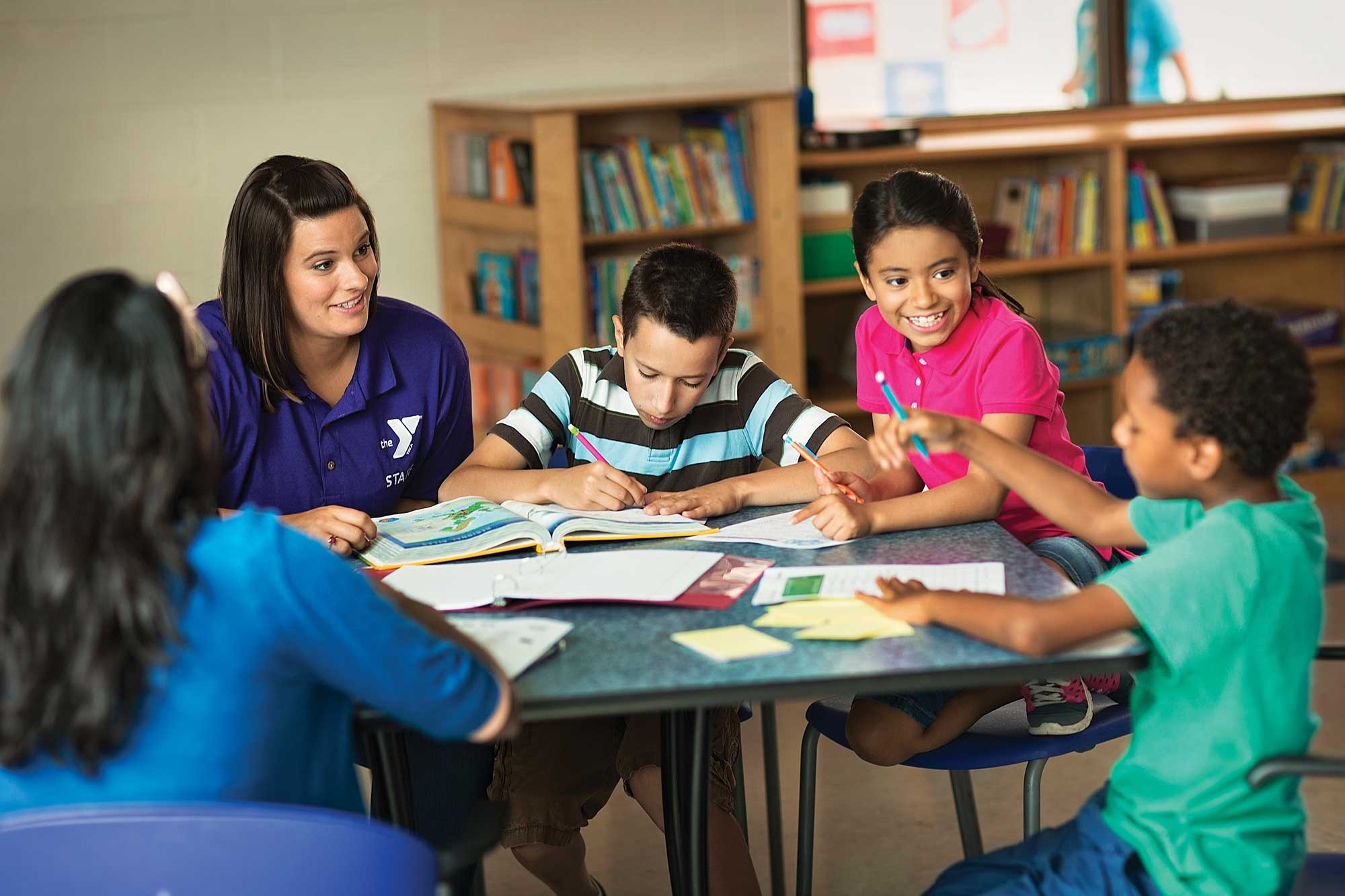 Teacher with four young kids at a table with open books.