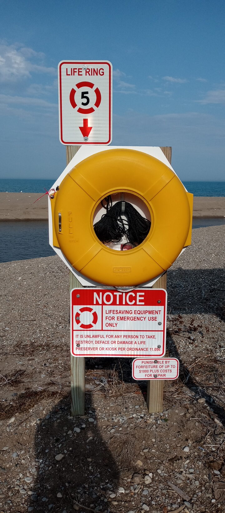 Yellow life preserver floatation device on wooden pole in the sand near the blue water