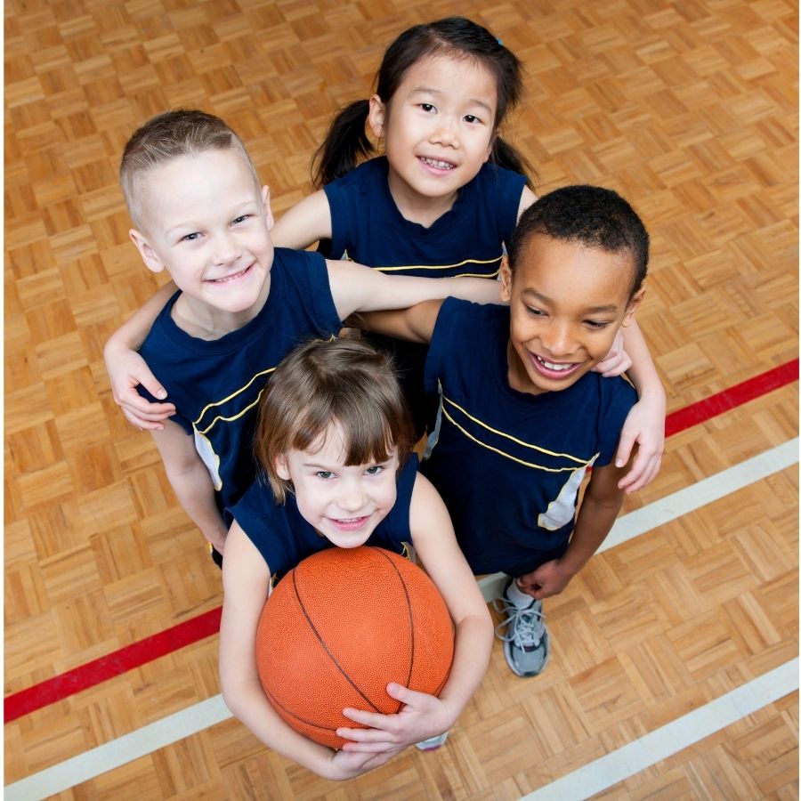 Four children on basketball court smiling for the camera.