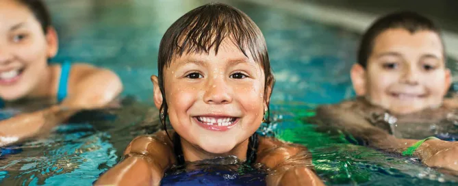 Three Smiling Children Swimming At The Ymca Pool At The Annual Luncheon.