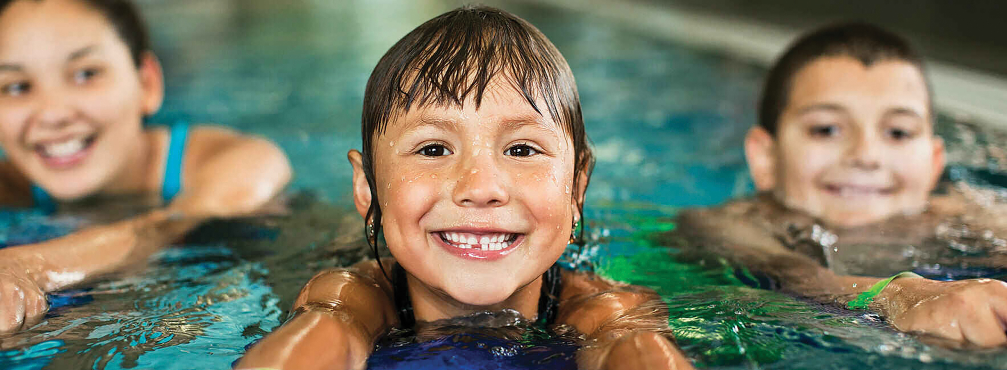 Three smiling children swimming at the YMCA pool at the Annual Luncheon.